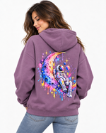 Woman wearing a mauve purple hoodie with large rainbow astronaut on crescent moon back graphic