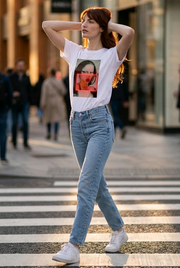 Woman walking on a crosswalk wearing a white t-shirt with a graphic design and light blue jeans.
